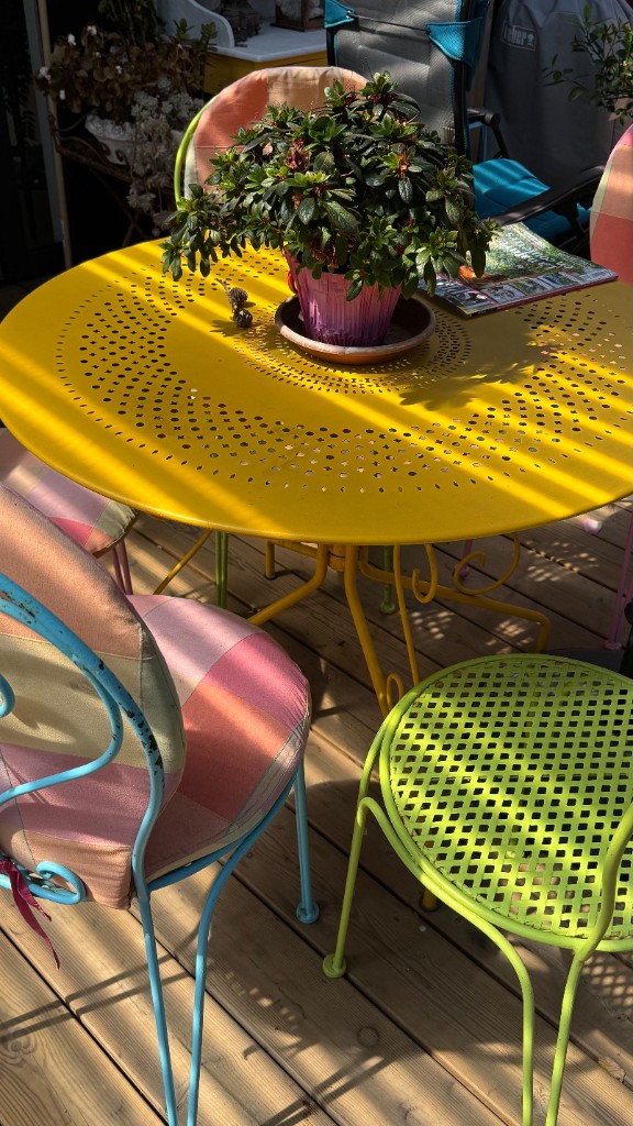 Gelber Gartentisch mit Kübelpflanze auf einer Holzterrasse
